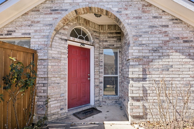 view of exterior entry with fence and brick siding