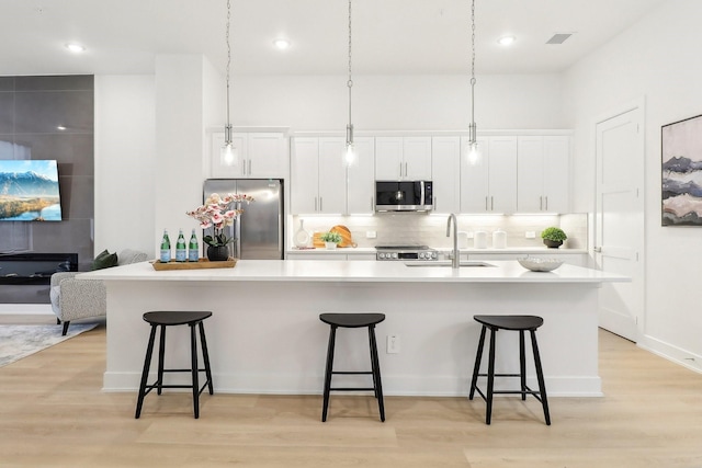 kitchen with appliances with stainless steel finishes, light wood-type flooring, white cabinets, and a sink