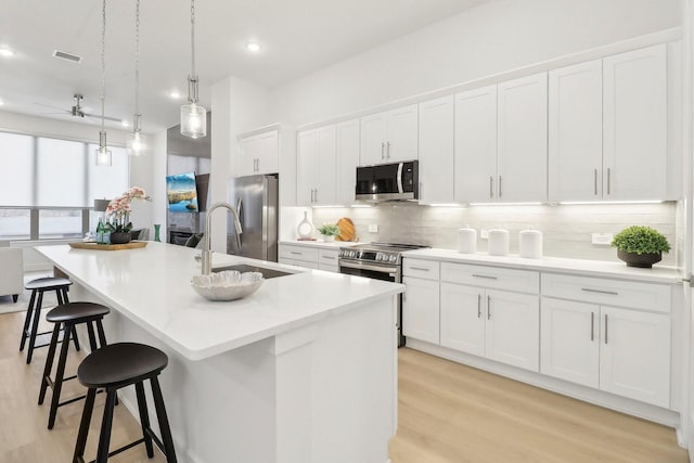 kitchen with visible vents, white cabinets, appliances with stainless steel finishes, a kitchen island with sink, and backsplash