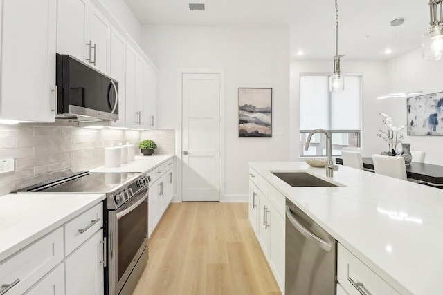 kitchen featuring stainless steel appliances, a sink, light wood-style floors, light countertops, and backsplash