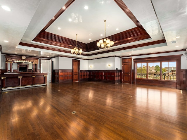 unfurnished living room with visible vents, a wainscoted wall, a tray ceiling, dark wood-type flooring, and a chandelier