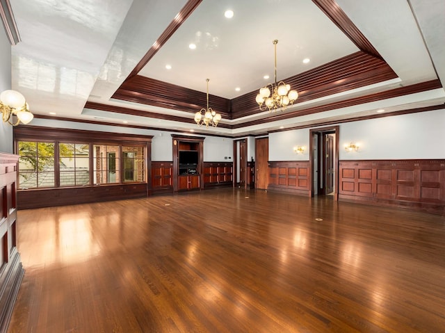 unfurnished living room with a tray ceiling, wood finished floors, wainscoting, and a chandelier