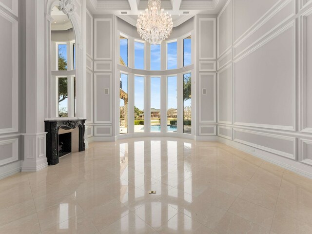 unfurnished living room with an inviting chandelier, a decorative wall, a towering ceiling, and ornamental molding