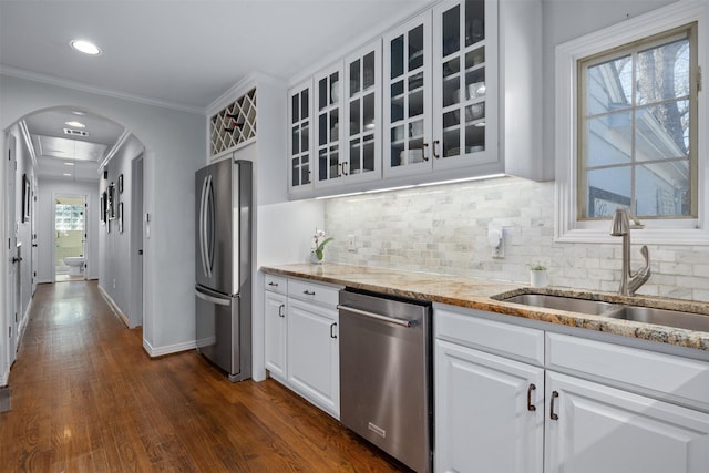 kitchen with arched walkways, a sink, ornamental molding, appliances with stainless steel finishes, and glass insert cabinets