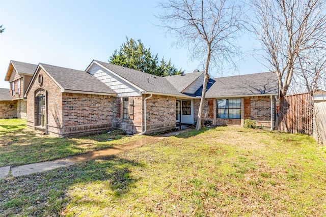 single story home with brick siding, a front yard, fence, and a shingled roof