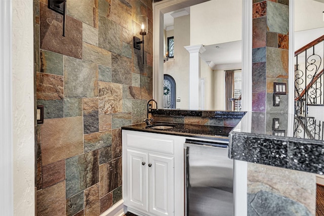 interior space featuring crown molding, white cabinetry, a sink, dark stone countertops, and ornate columns