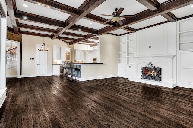 unfurnished living room featuring baseboards, dark wood finished floors, coffered ceiling, beam ceiling, and ceiling fan with notable chandelier