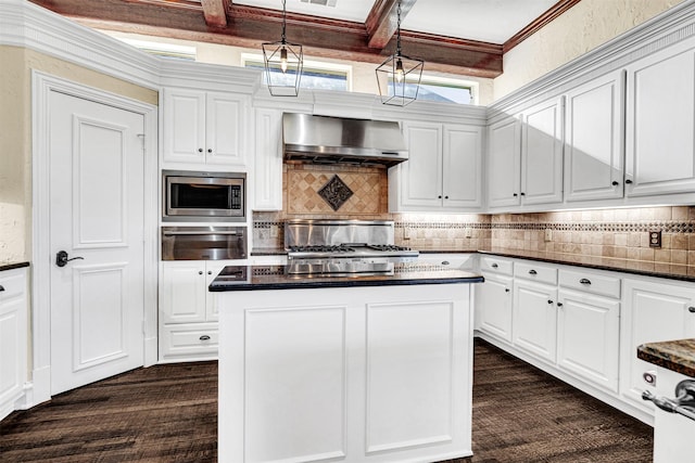 kitchen with wall chimney range hood, stainless steel microwave, white cabinets, and beamed ceiling