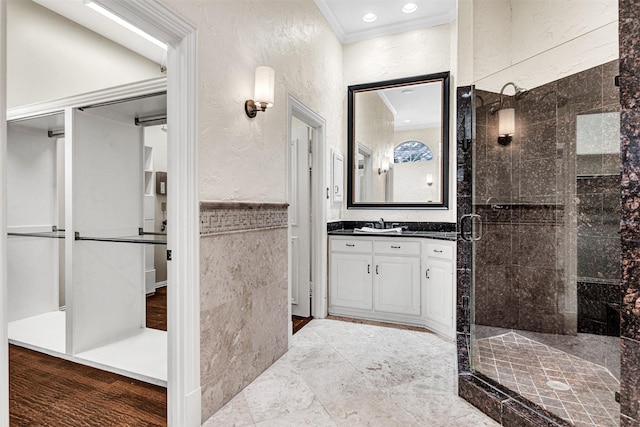 full bathroom with a stall shower, a textured wall, ornamental molding, vanity, and tile walls