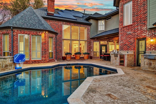 rear view of property with brick siding, a chimney, area for grilling, a patio area, and an outdoor pool