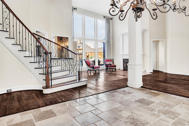 entryway with baseboards, decorative columns, stone tile floors, and an inviting chandelier