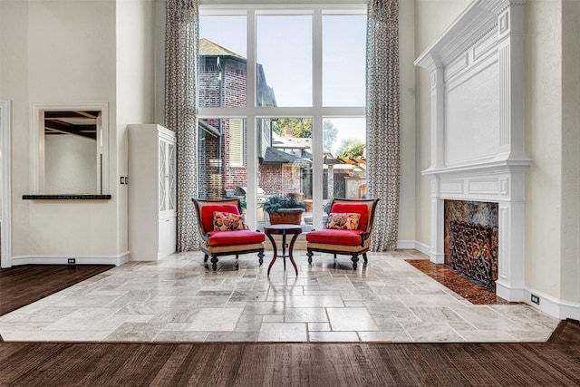 sitting room featuring stone tile flooring, a fireplace, a towering ceiling, and baseboards