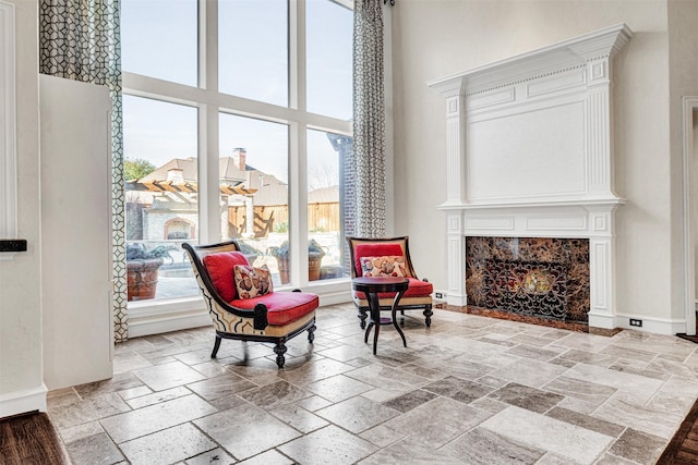 sitting room featuring baseboards, a premium fireplace, a high ceiling, and stone tile flooring