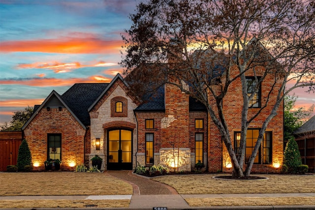 view of front of property featuring stone siding, brick siding, roof with shingles, and french doors