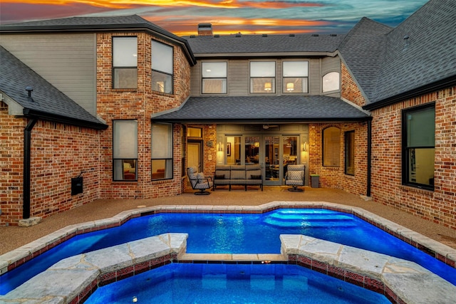 back of house with a pool with connected hot tub, a shingled roof, a patio area, and brick siding