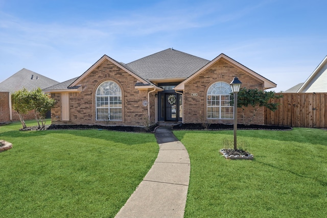 ranch-style house featuring a shingled roof, a front yard, fence, and brick siding