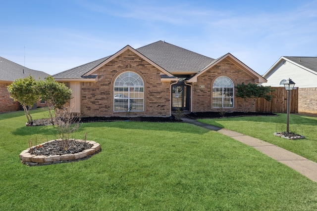 ranch-style house featuring roof with shingles, brick siding, a front lawn, and fence