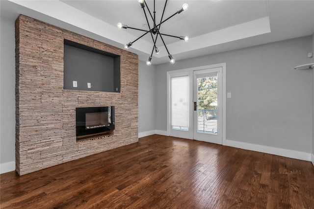 unfurnished living room featuring baseboards, a raised ceiling, wood finished floors, and a stone fireplace