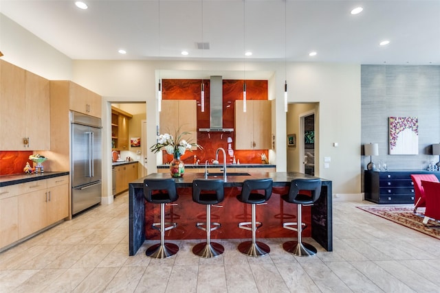 kitchen featuring wall chimney exhaust hood, a breakfast bar, built in refrigerator, and a sink