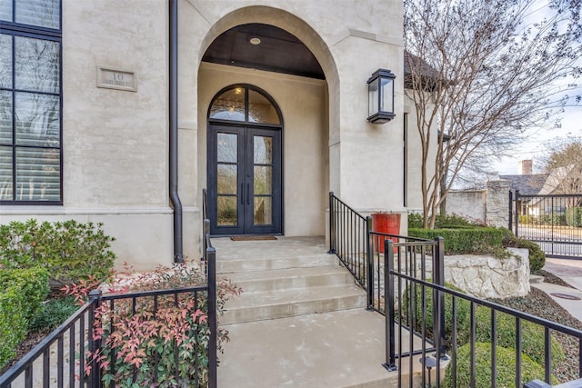 property entrance featuring stucco siding, fence, and french doors