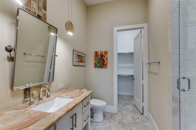 bathroom with toilet, vanity, baseboards, a spacious closet, and a shower with door