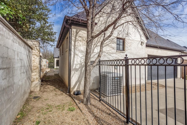 view of property exterior featuring a shingled roof, fence, and central air condition unit