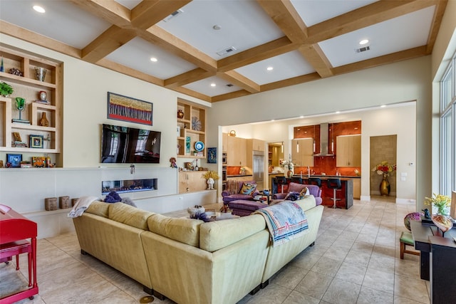 living area with a glass covered fireplace, beam ceiling, coffered ceiling, and visible vents