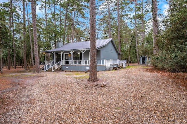 view of front of home featuring a chimney, covered porch, metal roof, a shed, and an outdoor structure