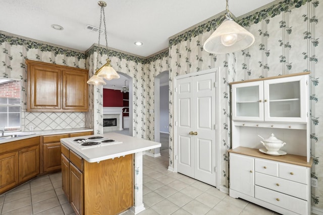 kitchen with wallpapered walls, white electric stovetop, arched walkways, brown cabinets, and light countertops