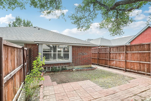 exterior space with a fenced backyard, roof with shingles, a patio, and brick siding