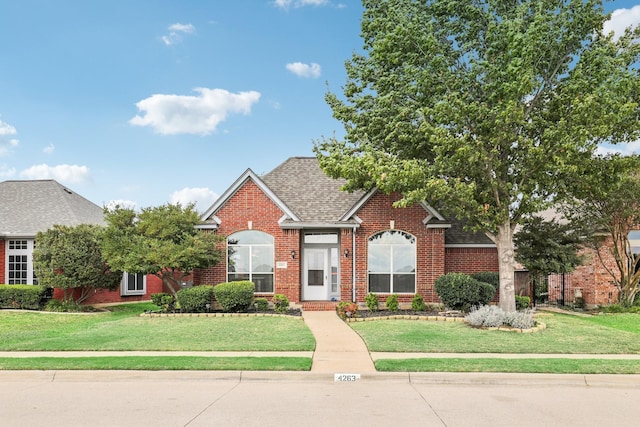 view of front of property featuring brick siding, roof with shingles, and a front yard