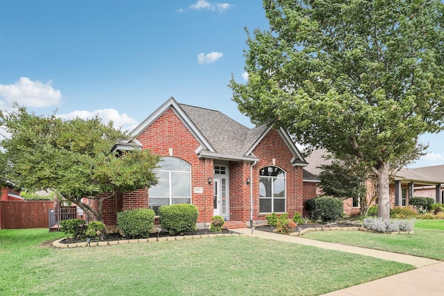 traditional home with roof with shingles, brick siding, a front lawn, and fence