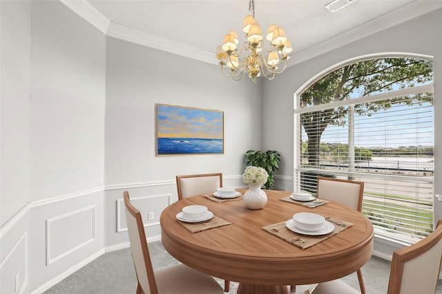 carpeted dining space featuring a chandelier, a wainscoted wall, ornamental molding, and a decorative wall