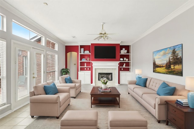 living area with built in features, a fireplace, crown molding, light tile patterned floors, and a ceiling fan