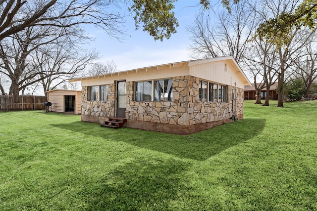 rear view of house featuring entry steps, stone siding, fence, and a lawn