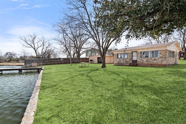 view of yard featuring a dock, a water view, fence, and an outdoor structure