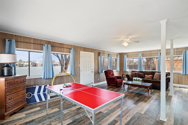 playroom featuring wooden walls, baseboards, ceiling fan, dark wood-style flooring, and a water view