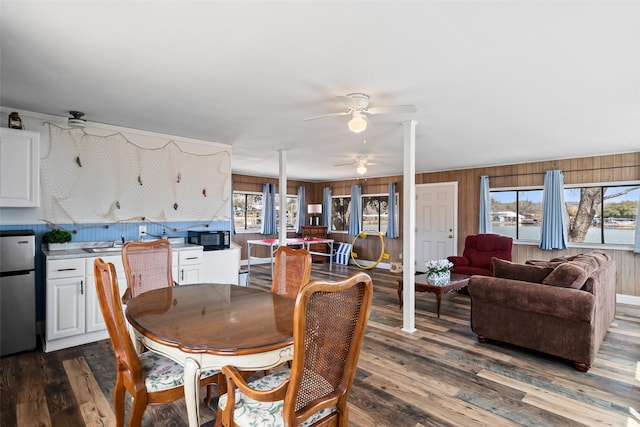 dining room with dark wood-style floors, wood walls, and a ceiling fan