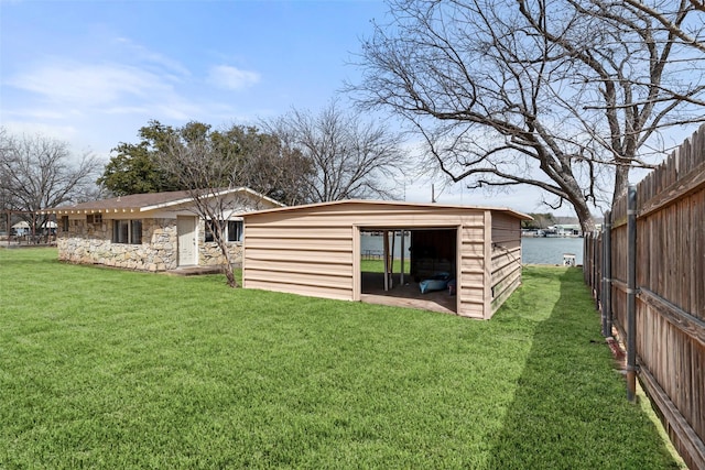 rear view of property with an outdoor structure, fence, a water view, a yard, and stone siding