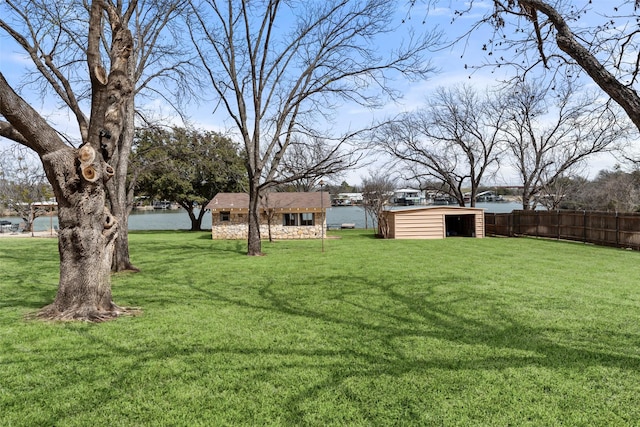 view of yard featuring a water view, fence, and an outdoor structure