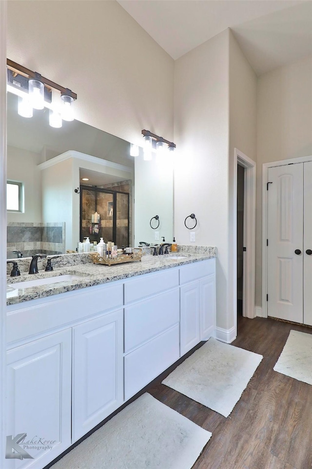 full bathroom with a stall shower, double vanity, a sink, and wood finished floors