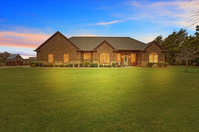 french country style house with brick siding, a lawn, and a shingled roof