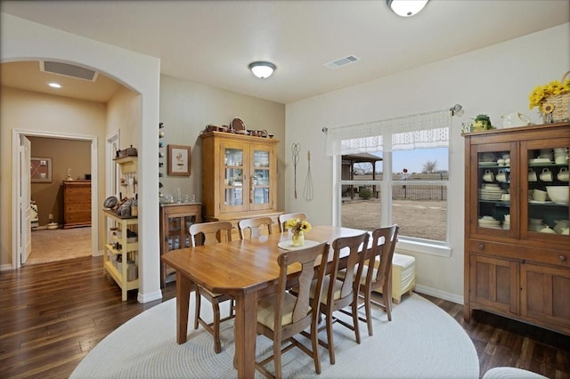 dining area featuring arched walkways, dark wood-style flooring, visible vents, and baseboards