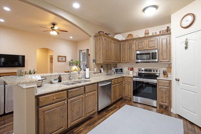 kitchen with arched walkways, stainless steel appliances, a peninsula, a sink, and dark wood finished floors