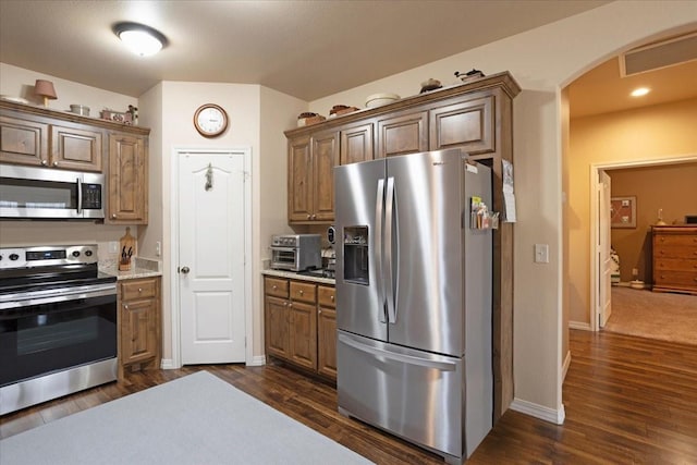 kitchen with arched walkways, dark wood finished floors, stainless steel appliances, visible vents, and baseboards