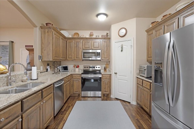 kitchen featuring a toaster, dark wood-type flooring, a sink, appliances with stainless steel finishes, and light stone countertops