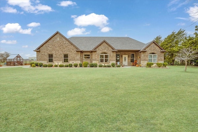 french country home with a shingled roof, a front yard, and brick siding