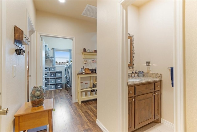 corridor featuring independent washer and dryer, wood finished floors, visible vents, and baseboards