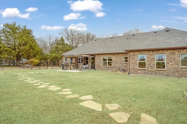 rear view of property featuring brick siding, roof with shingles, a patio area, and fence