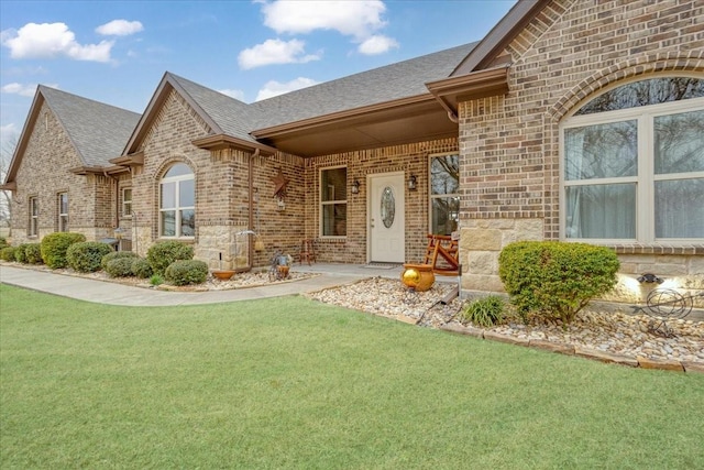 doorway to property featuring stone siding, brick siding, a yard, and roof with shingles